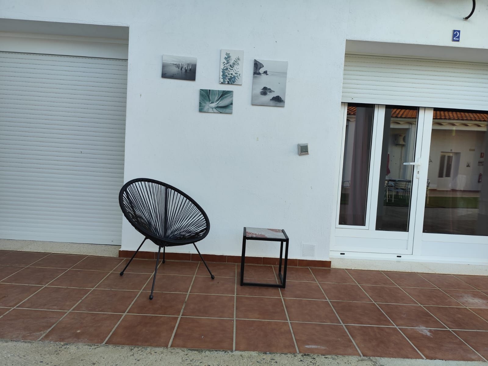 Una silla negra se encuentra en un patio de baldosas frente a una pared blanca.