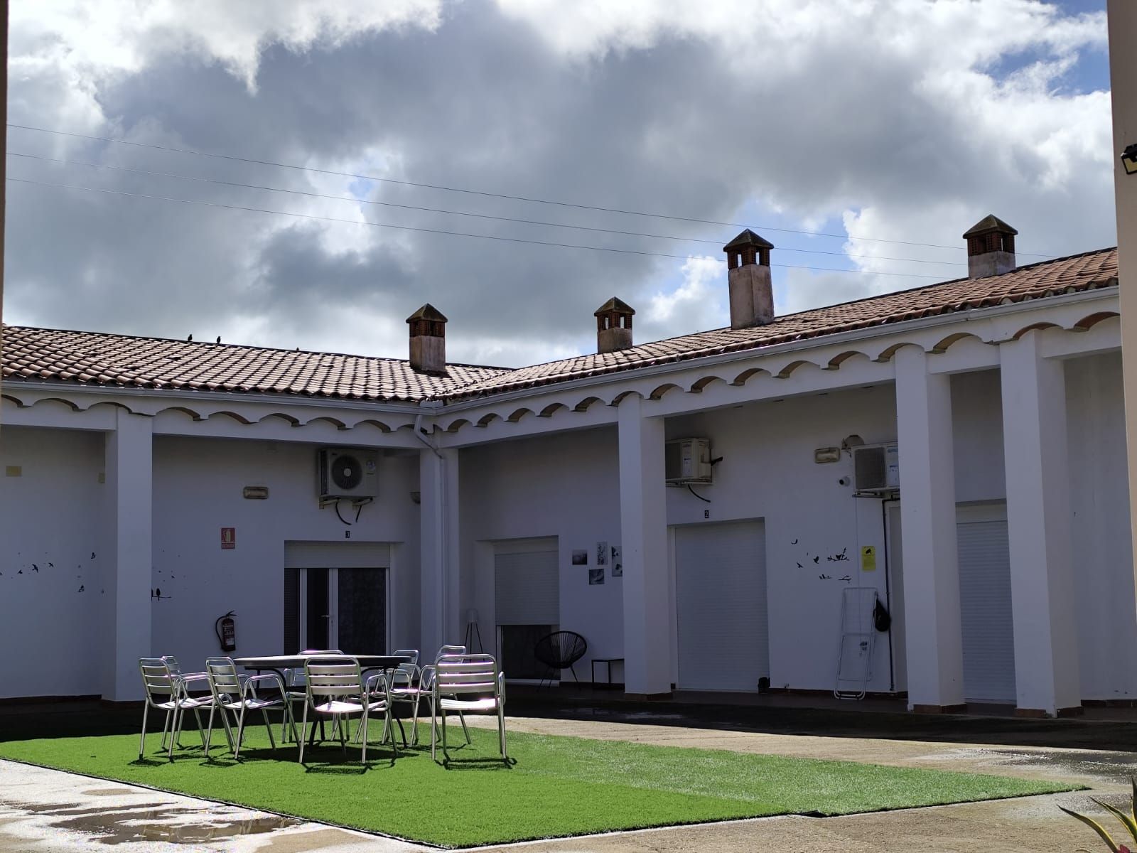 Un patio con mesas y sillas frente a un edificio blanco.