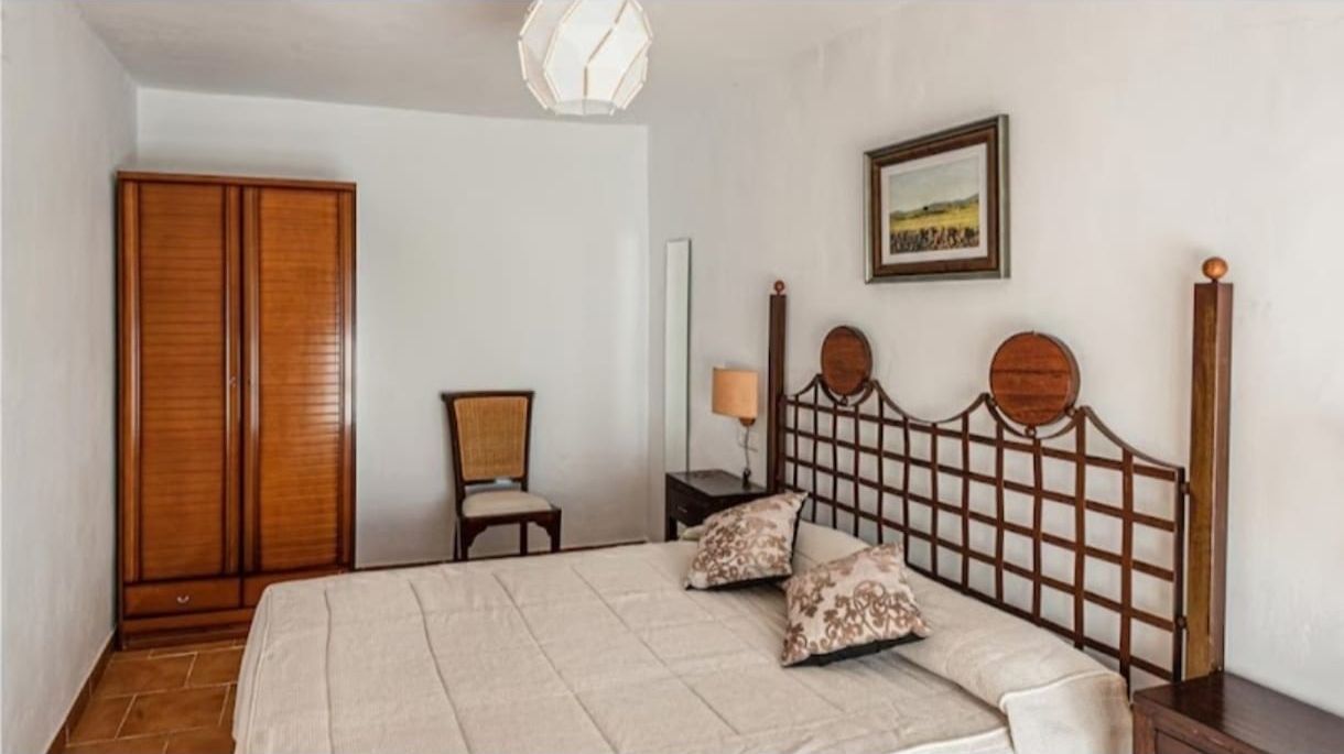 Un dormitorio con una cama grande, una silla, un armario y un cuadro en la pared.