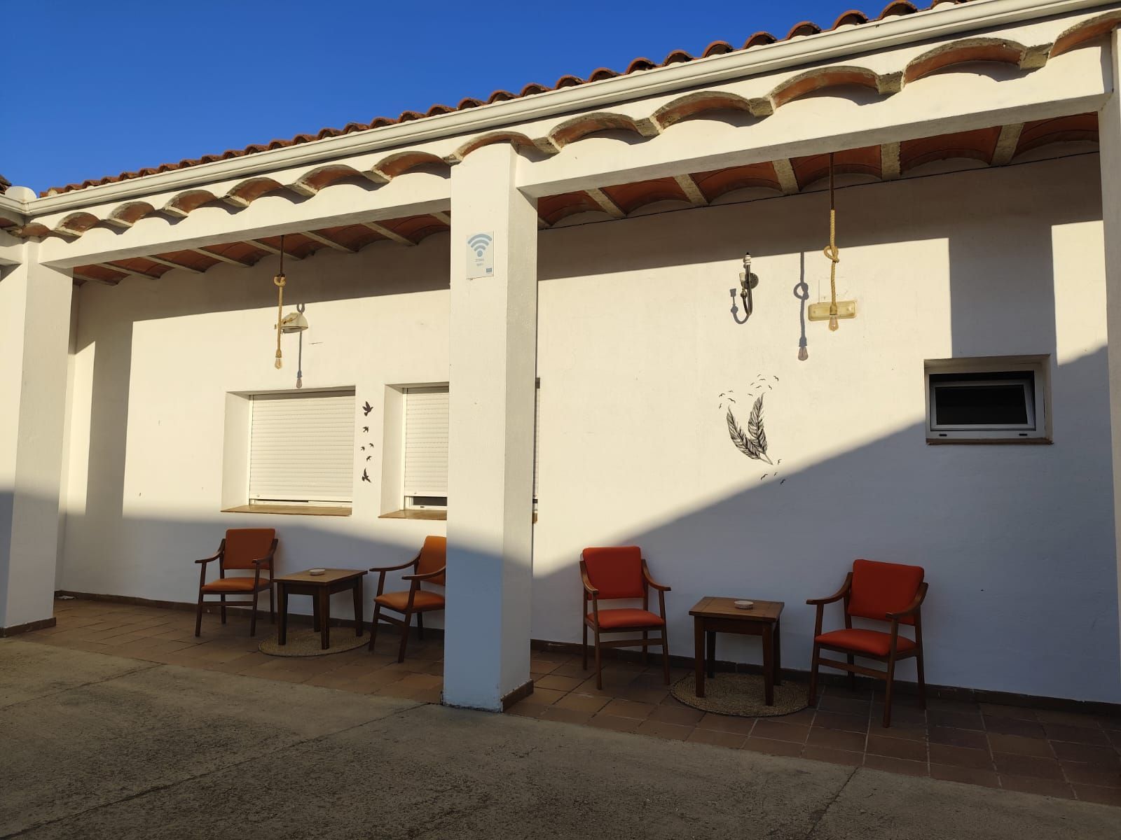 Un edificio blanco con sillas y mesas rojas bajo un porche cubierto.