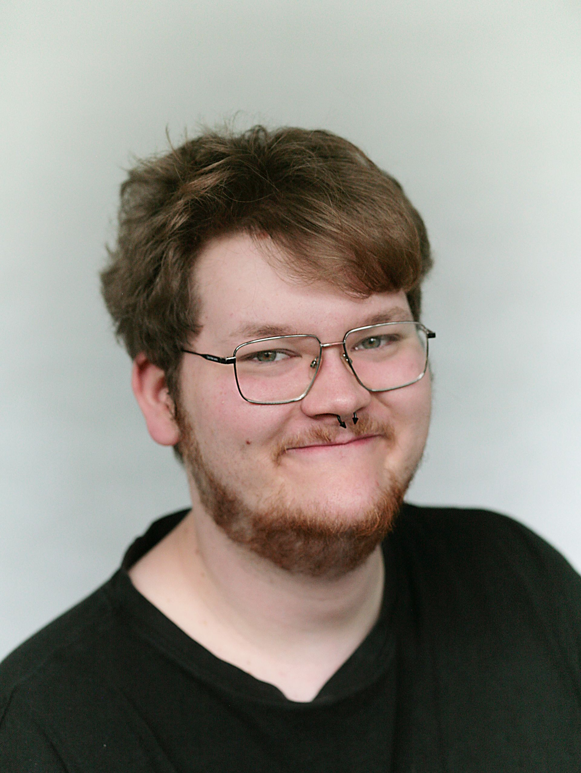 Porträt eines lächelnden Mannes mit dunklem Haar und Bart vor hellem Hintergrund