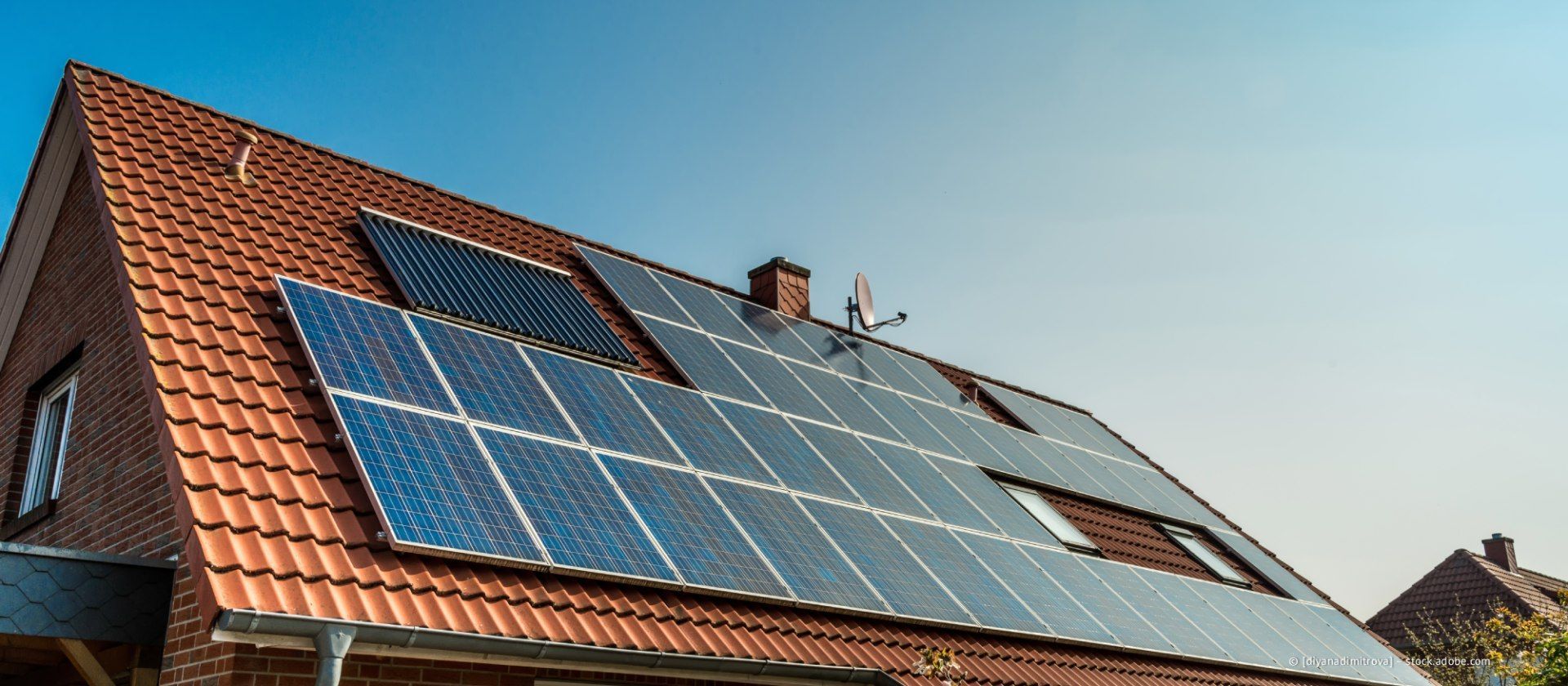 Solarpaneele, installiert auf einem rotziegelgedeckten Hausdach unter strahlend blauem Himmel.