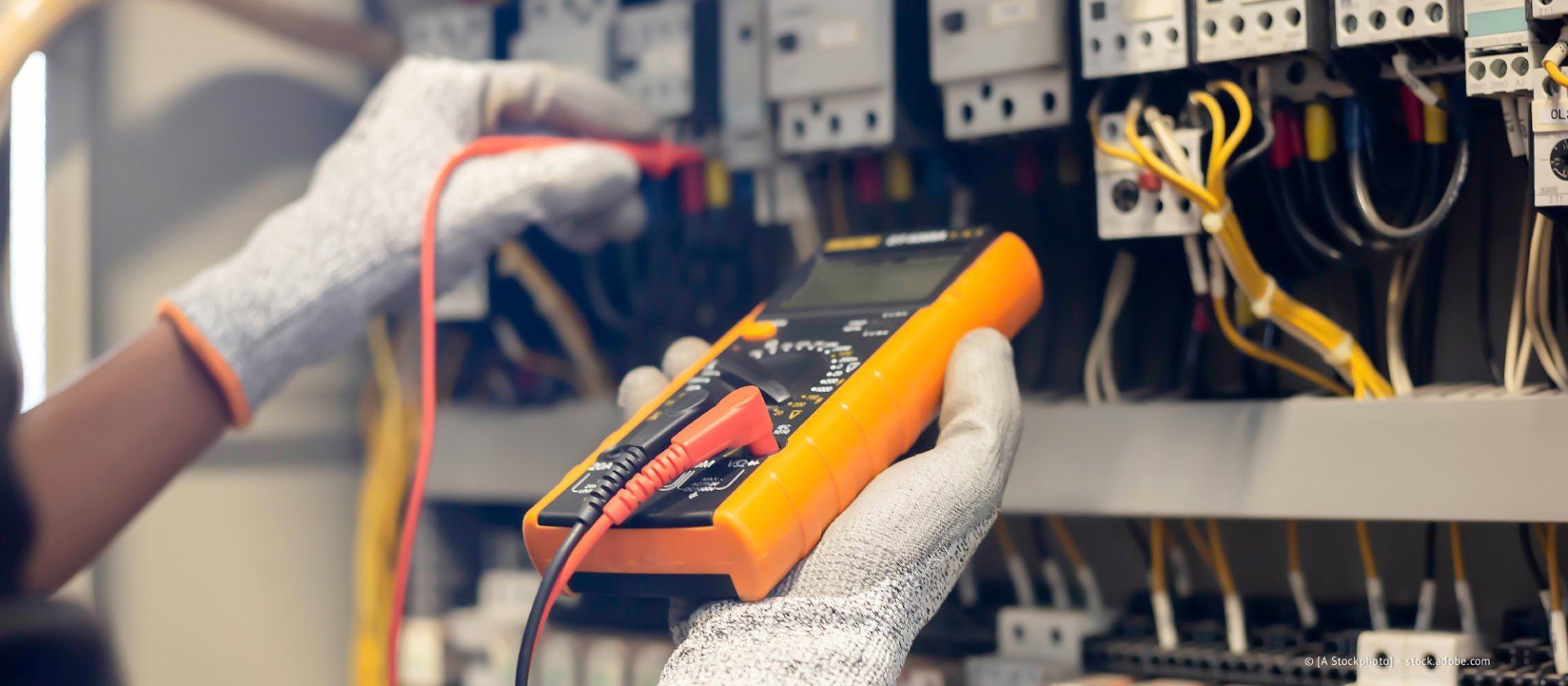 Ein Techniker mit Handschuhen überprüft mit einem Multimeter die elektrische Verkabelung in einem Schaltschrank.