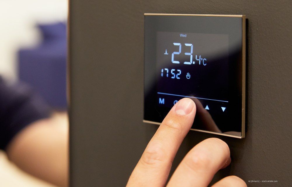 Finger justiert die Anzeige eines digitalen Thermostats, der 23,4 °C anzeigt, in einer Wohnumgebung