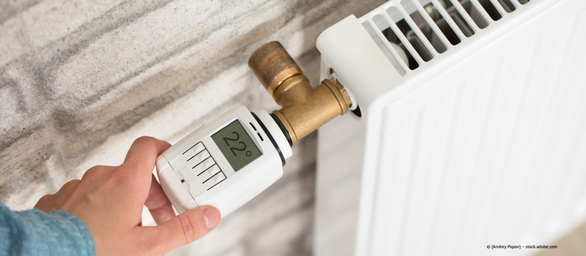 Manuelle Einstellung eines weißen Thermostats an einem Heizkörperventil neben einem an der Wand montierten Heizkörper.