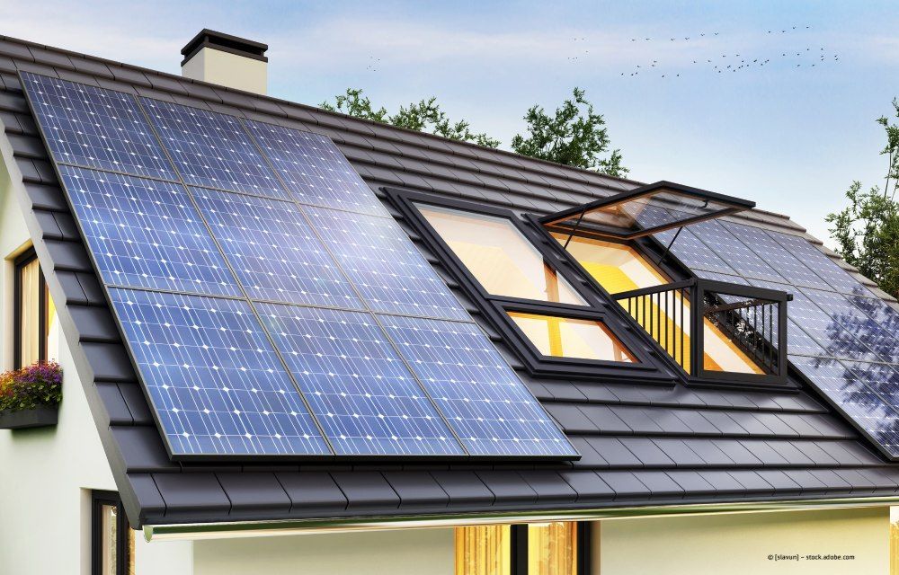 Hausdach mit großen Solarpaneelen und Dachfenstern unter blauem Himmel