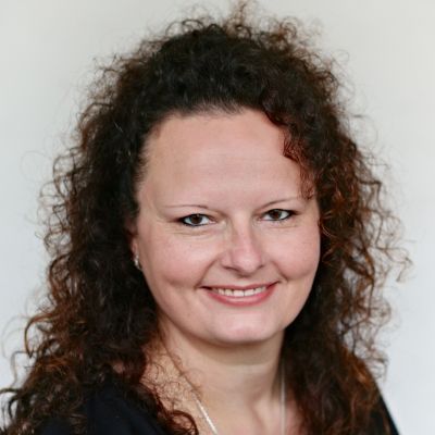 Porträt einer lächelnden Frau mit lockigem, dunklem Haar vor hellem Hintergrund