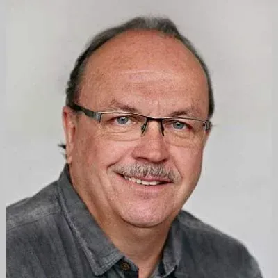 Porträt eines lächelnden Mannes mit Brille und grauem Hemd vor hellem Hintergrund