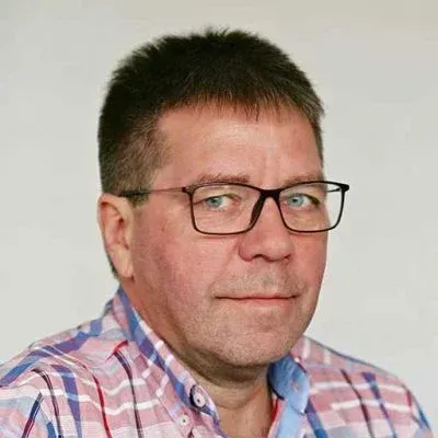 Porträt eines Mannes mit Brille und rosa kariertem Hemd vor einem einfarbigen, hellen Hintergrund