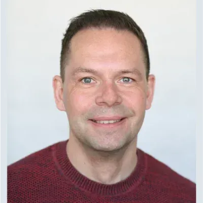 Lächelnder Mann in einem bordeauxroten Pullover vor hellem Hintergrund