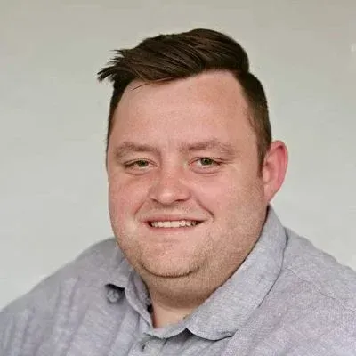 Porträt einer lächelnden Person in einem hellgrauen Poloshirt vor einem einfarbig grauen Hintergrund
