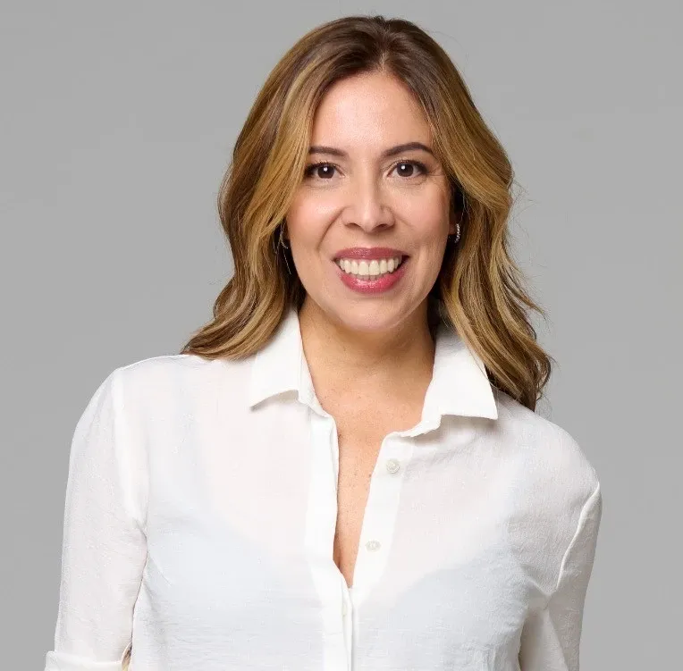 Varias personas se dan la mano sentadas a una mesa con un ordenador portátil, documentos y otra persona al fondo.