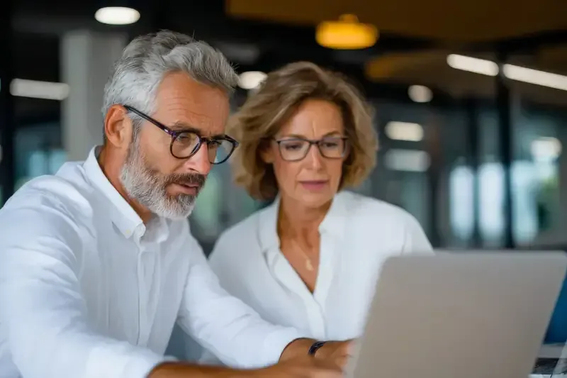 Hombre y mujer con gafas mirando una computadora portátil juntos en el interior.