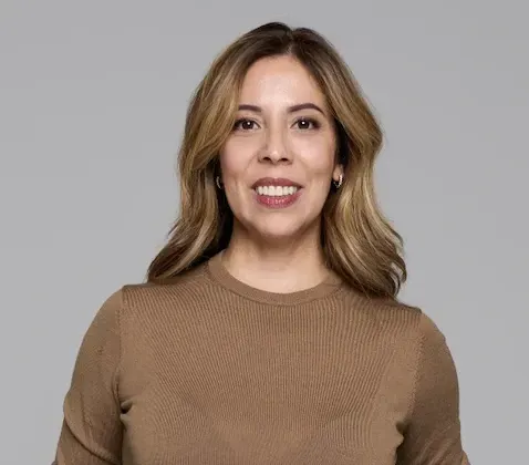 Varias personas se dan la mano sentadas a una mesa con un ordenador portátil, documentos y otra persona al fondo.