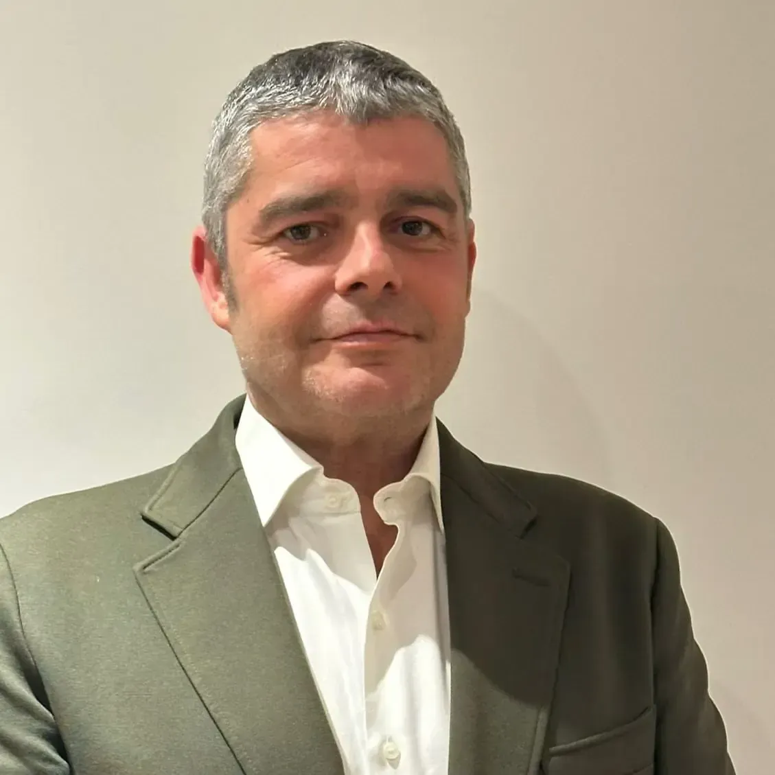 Hombre con traje oscuro, camisa blanca, corbata verde, mirando hacia adelante, expresión neutra.