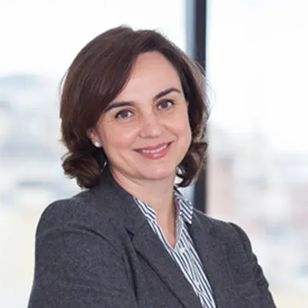 Mujer con blazer sonríe, cerca de la ventana.