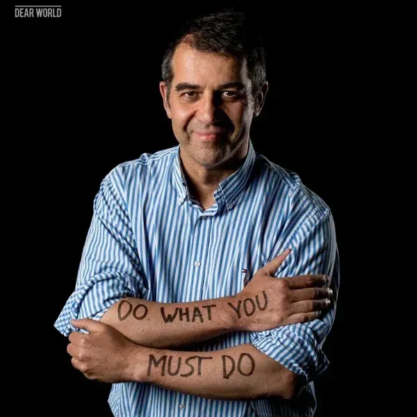 Hombre con los brazos cruzados. Lleva en los antebrazos un texto que dice 