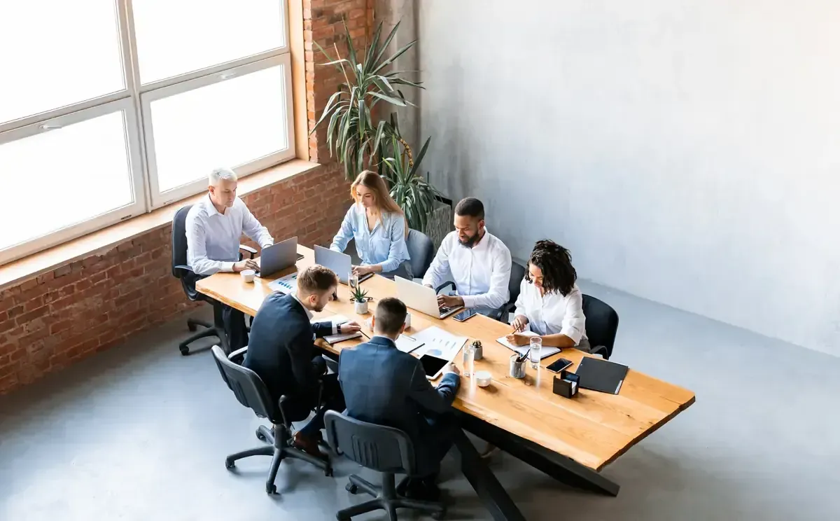 Grupo de personas en una larga mesa de madera, con computadoras portátiles abiertas.