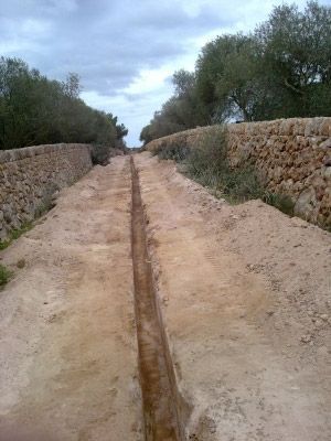 Un camino de tierra con un muro de piedra al costado.