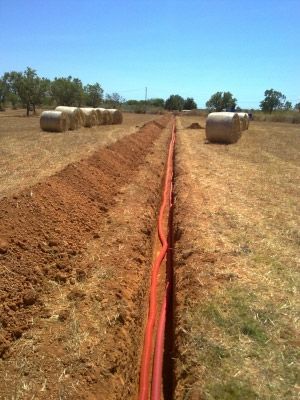 Una hilera de fardos de heno en un campo con una tubería roja en el medio.