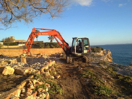 Una excavadora está sentada en la cima de una colina rocosa cerca del océano.