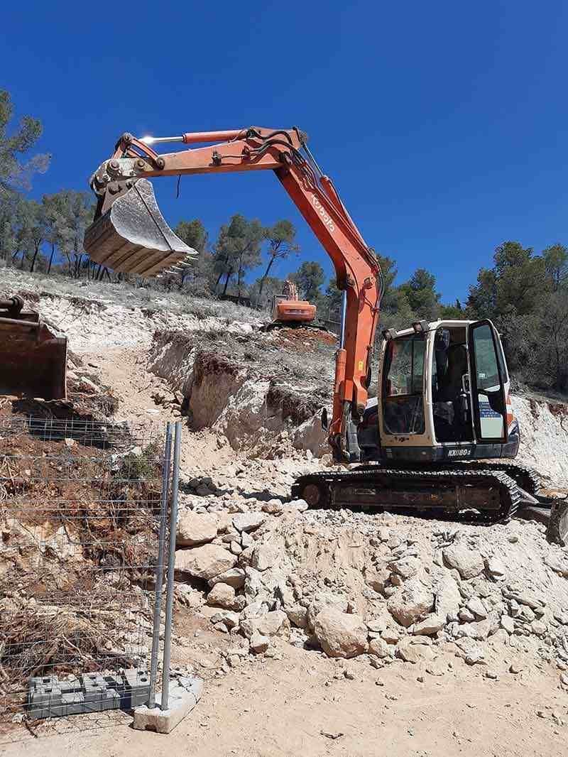 Una gran excavadora naranja está sentada en la cima de una colina rocosa.