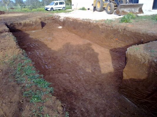 Un gran agujero en el suelo con una excavadora al fondo.