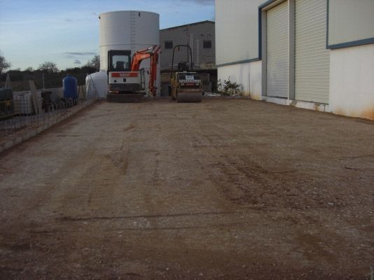 Una excavadora avanza por un camino de tierra frente a un edificio.