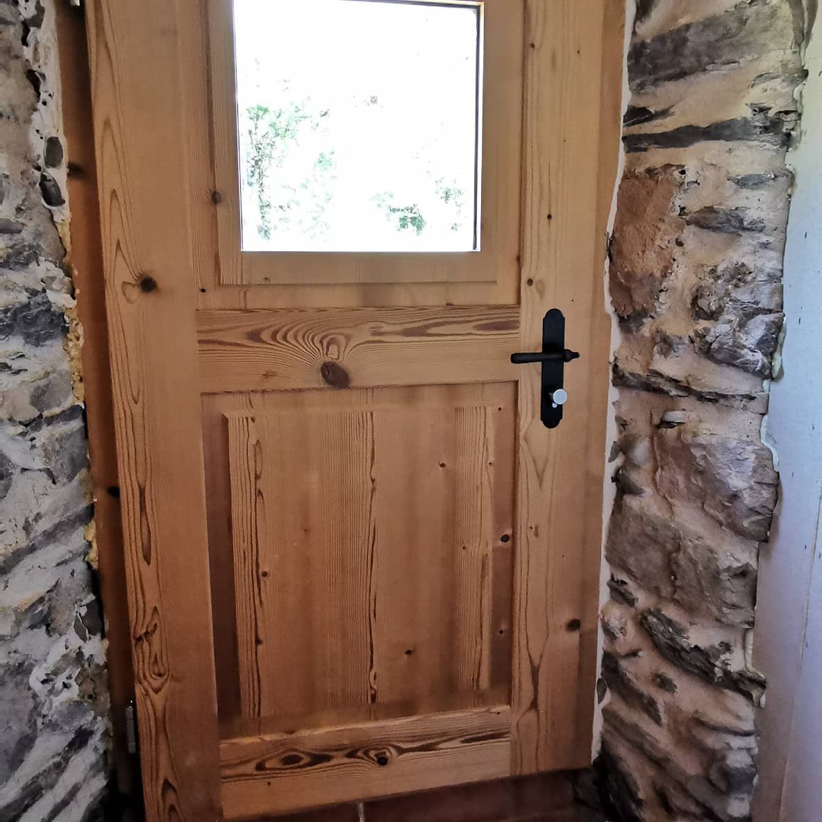 Une porte en bois avec une petite fenêtre dans un mur en pierre