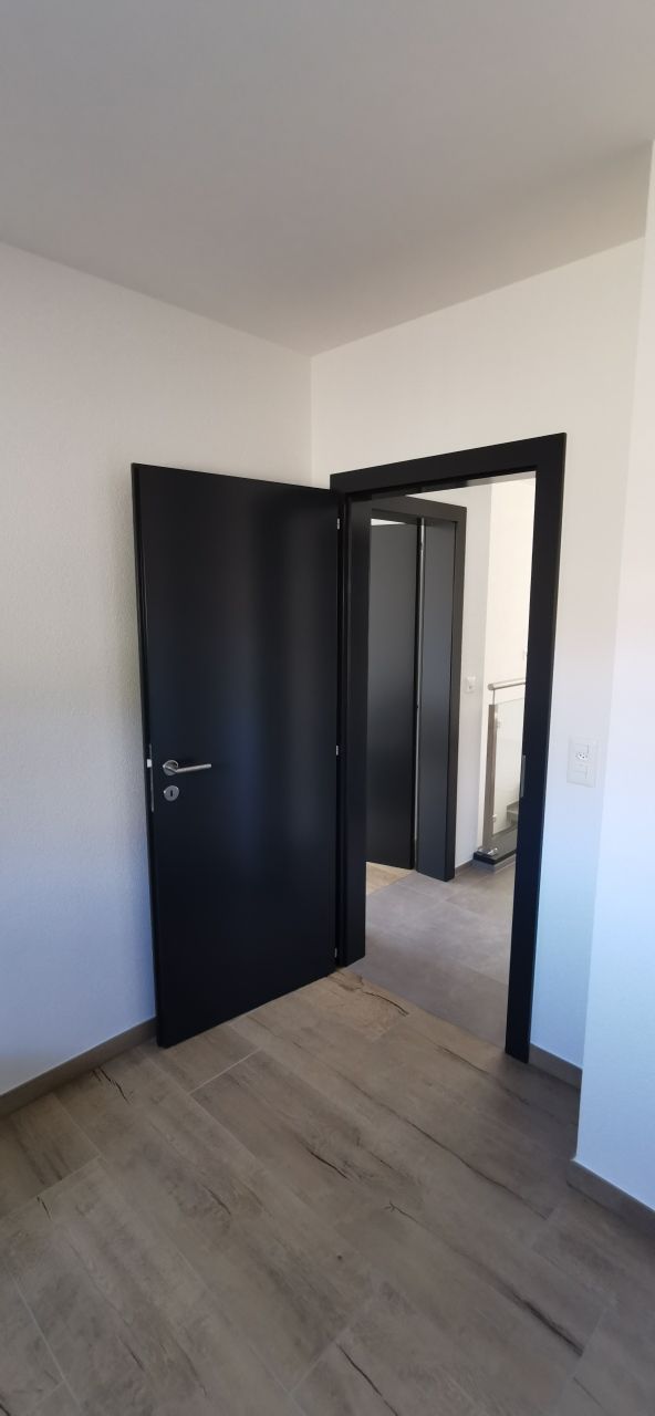 Une pièce vide avec une porte noire et un parquet en bois.