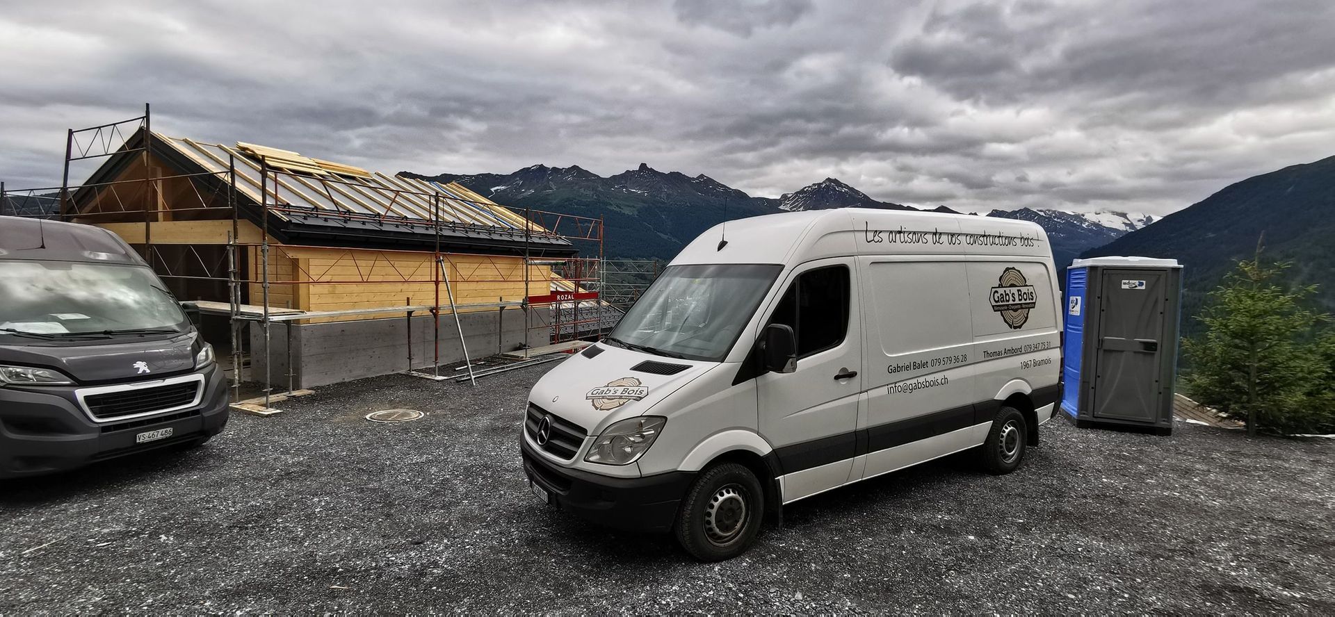 Deux camionnettes sont garées sur un terrain en gravier devant un immeuble en construction.