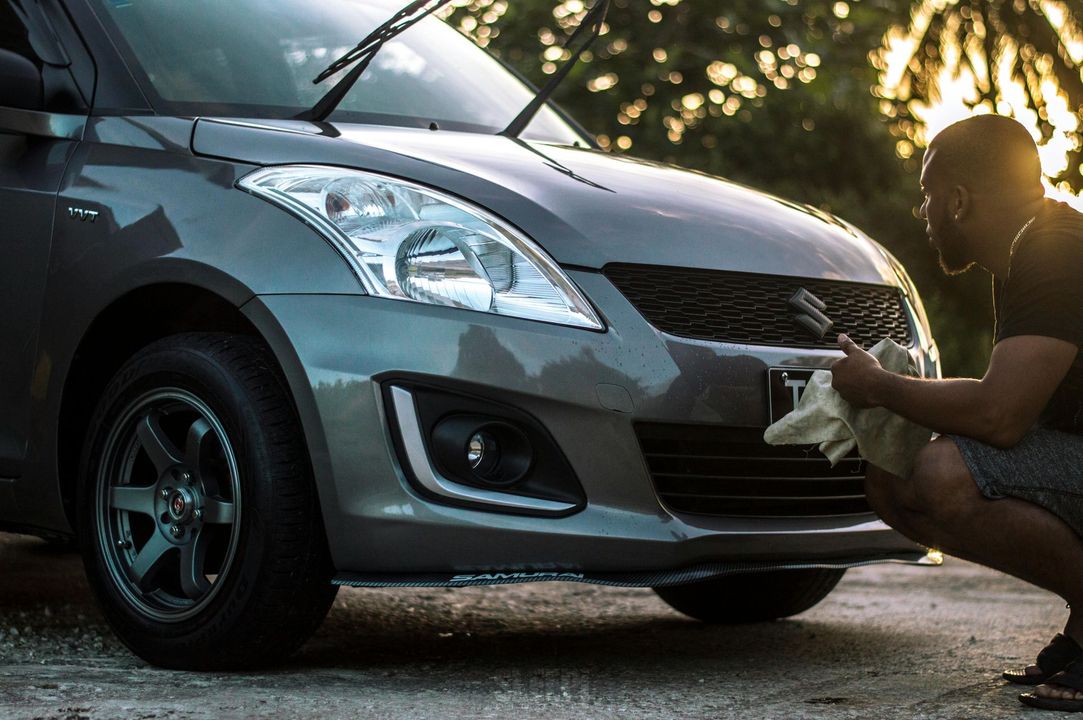 Hombre limpiando el frente de un automóvil Suzuki Swift gris al aire libre.