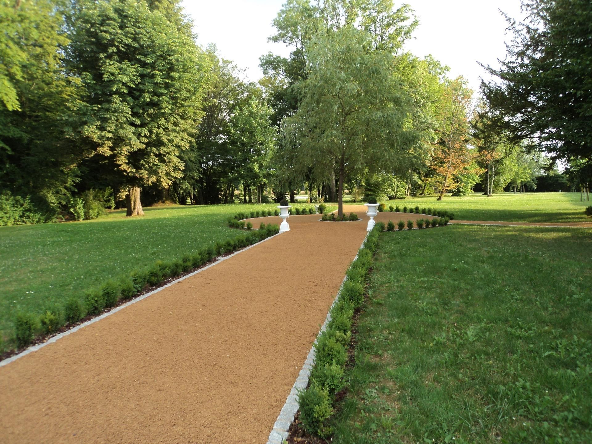 Chemin de gravier traversant un parc verdoyant bordé d'arbres et de pelouses tondues.
