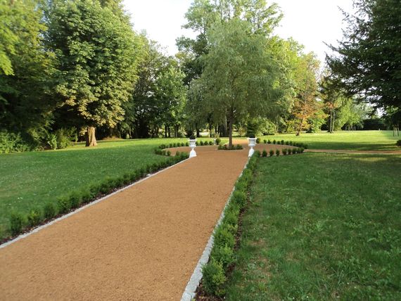 Chemin de gravier traversant un parc verdoyant bordé d'arbres et de pelouses tondues.