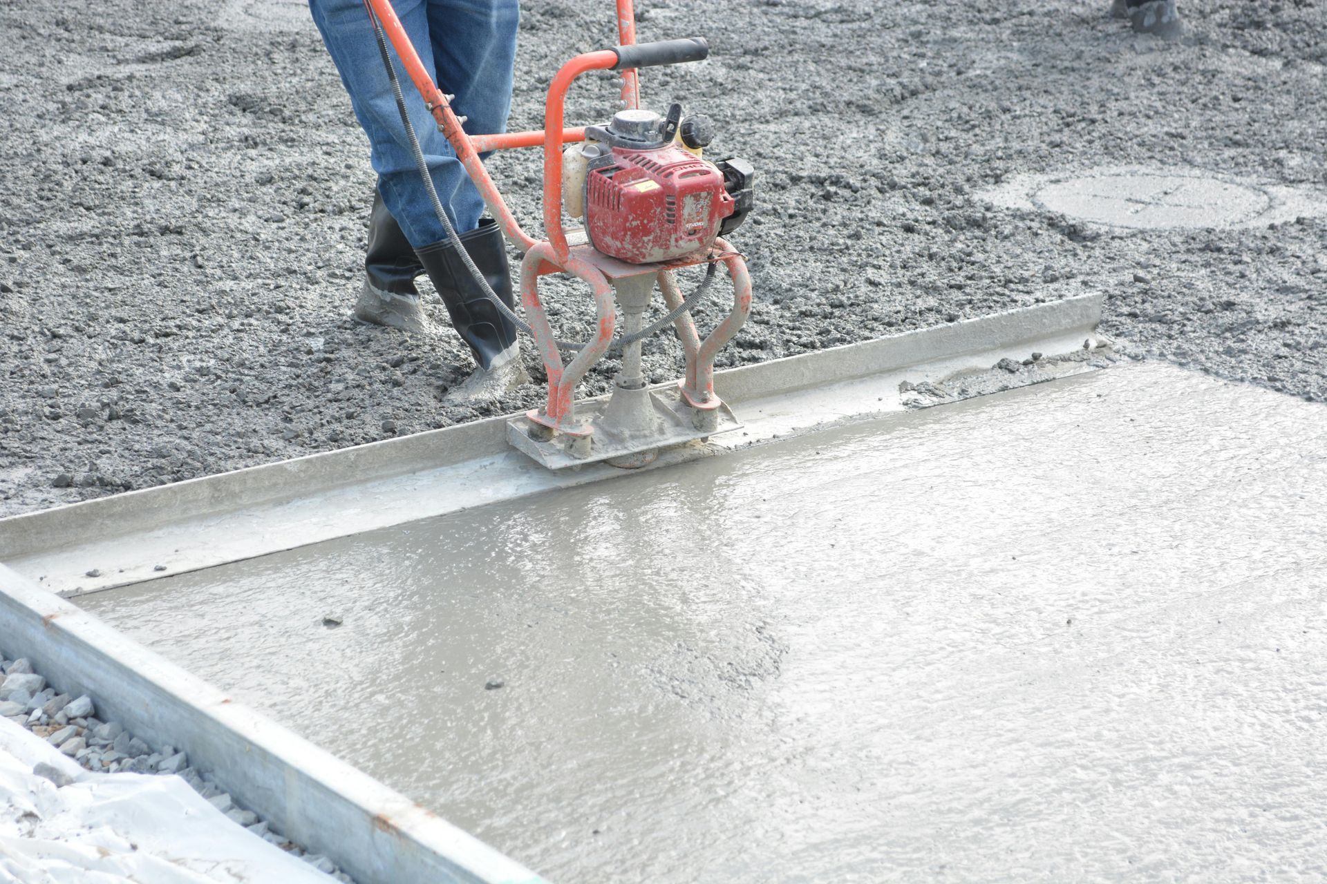 Ouvrier manipulant une règle à béton rouge pour niveler du béton gris frais sur un chantier de construction