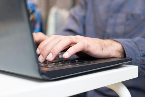 Des mains tapant sur un ordinateur portable à une table blanche
