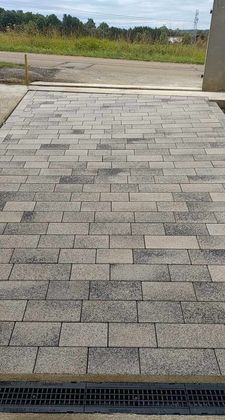 Allée pavée menant à une clairière herbeuse, avec une grille d'égout au premier plan.