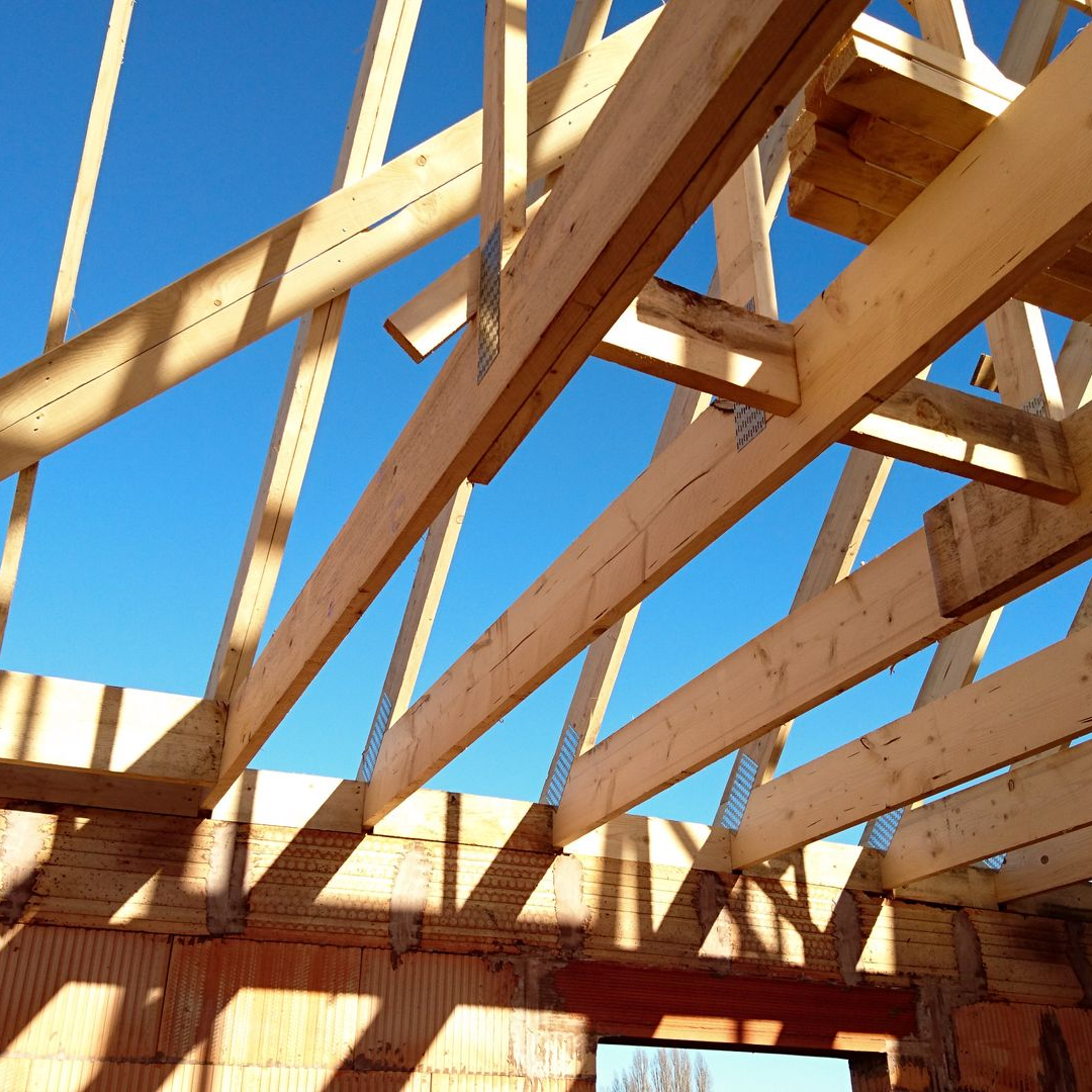 Charpente de toit en bois en construction, sur fond de ciel bleu.