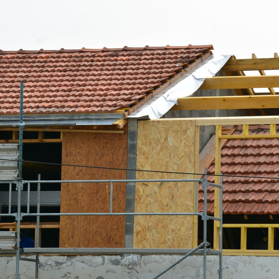 Construction d'un toit de maison, montrant la charpente en bois, les tuiles et les échafaudages.