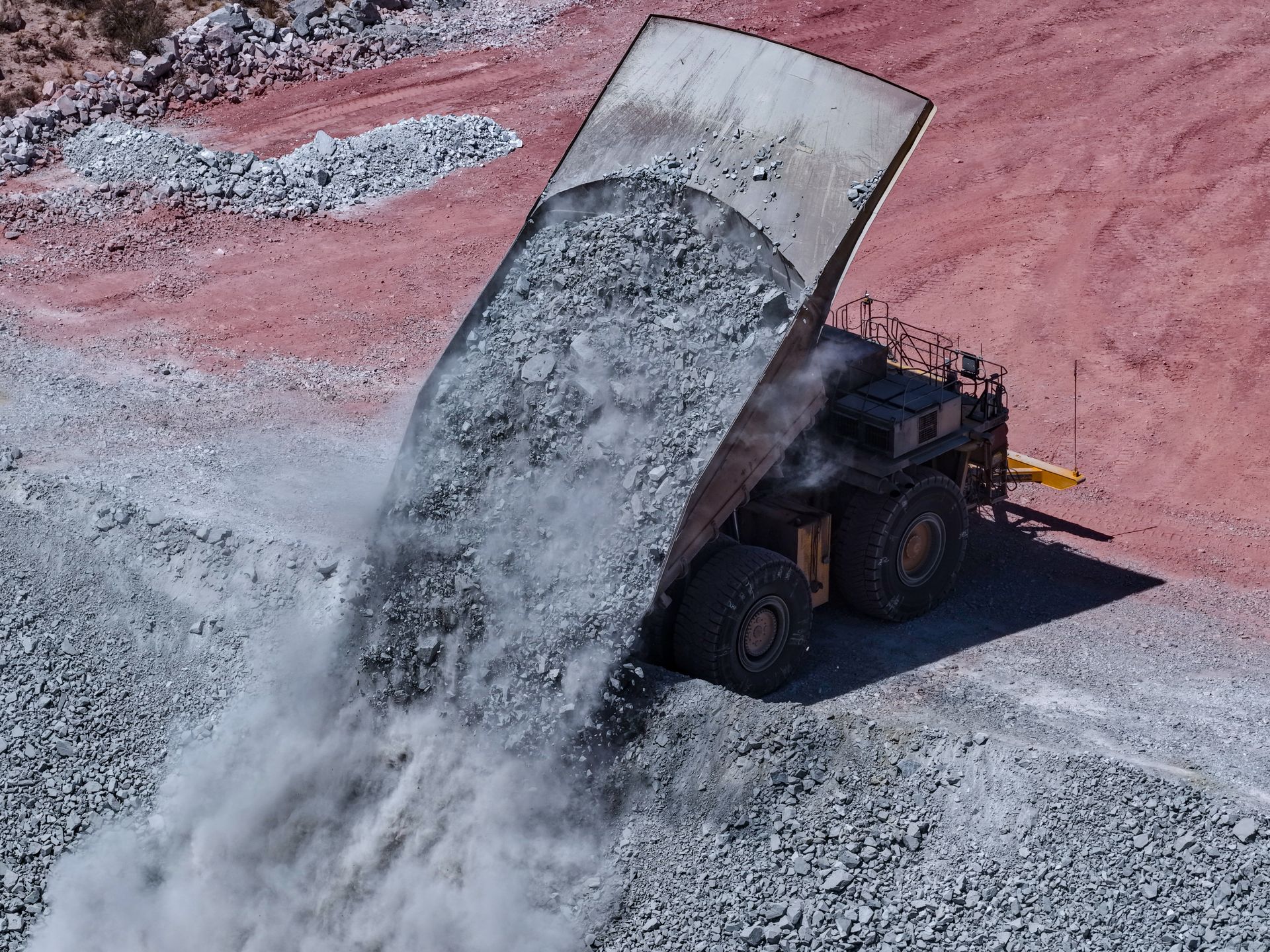 Un gros camion-benne déverse une cargaison de roches grises dans une fosse sur un site minier, sur fond de sol brun rougeâtre.