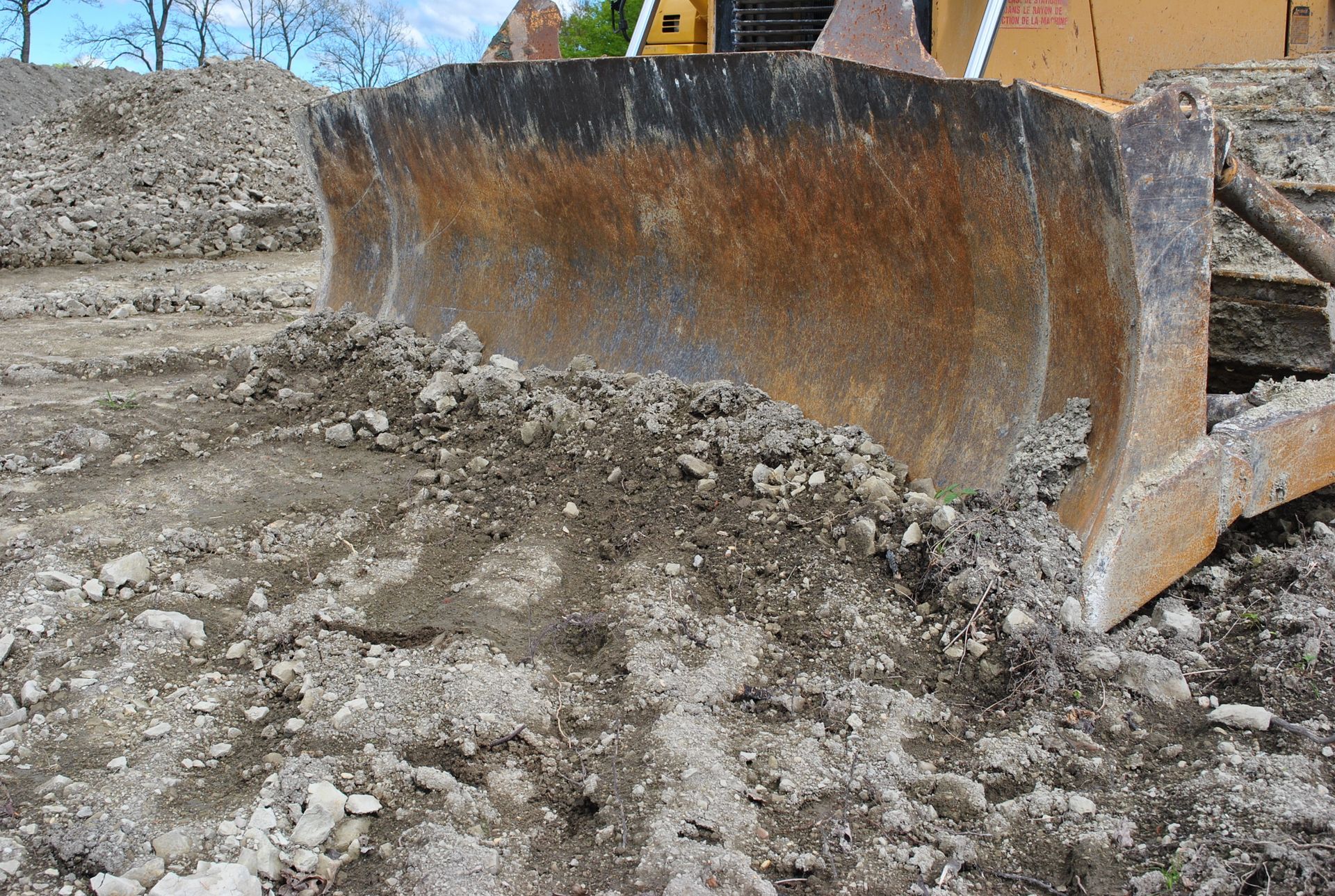 Gros plan sur la lame rouillée d'un bulldozer poussant un tas de terre rocailleuse sur un chantier de construction.