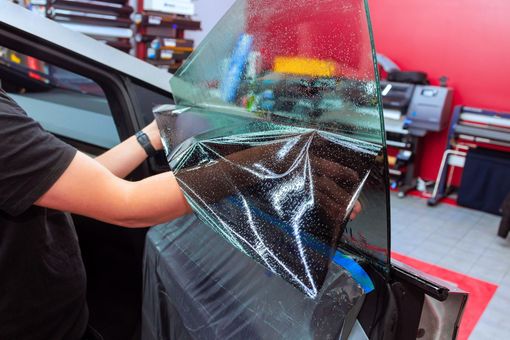 Un car detailer qui pose un film teinté sur une vitre de voiture.