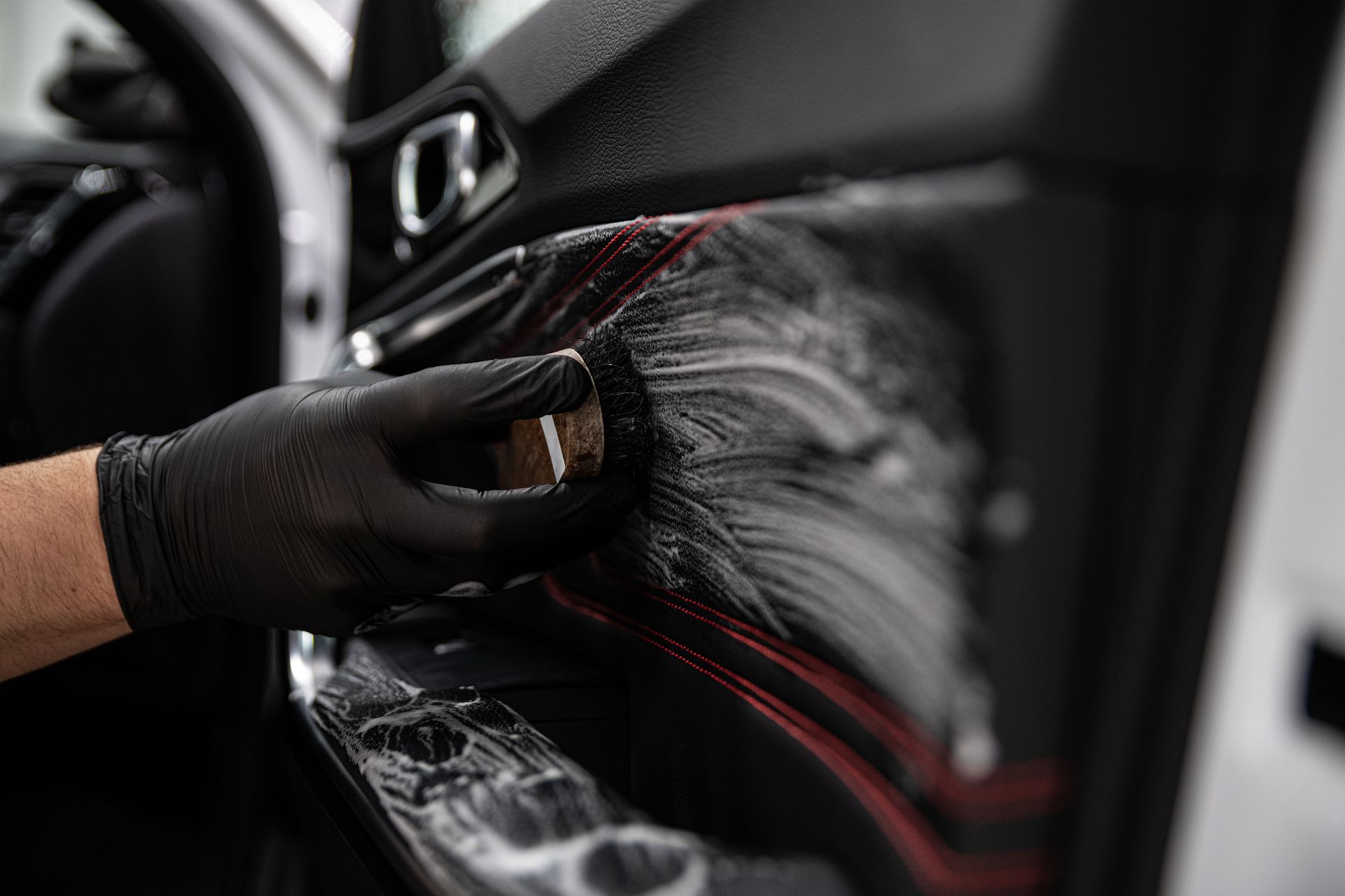 Gros plan sur un car detailer qui utilise une brosse pour nettoyer les tissus à l'intérieur d'une porte de voiture.