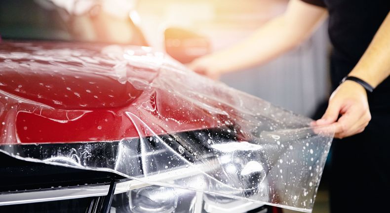 Un car detailer qui pose un PPF sur une voiture rouge.