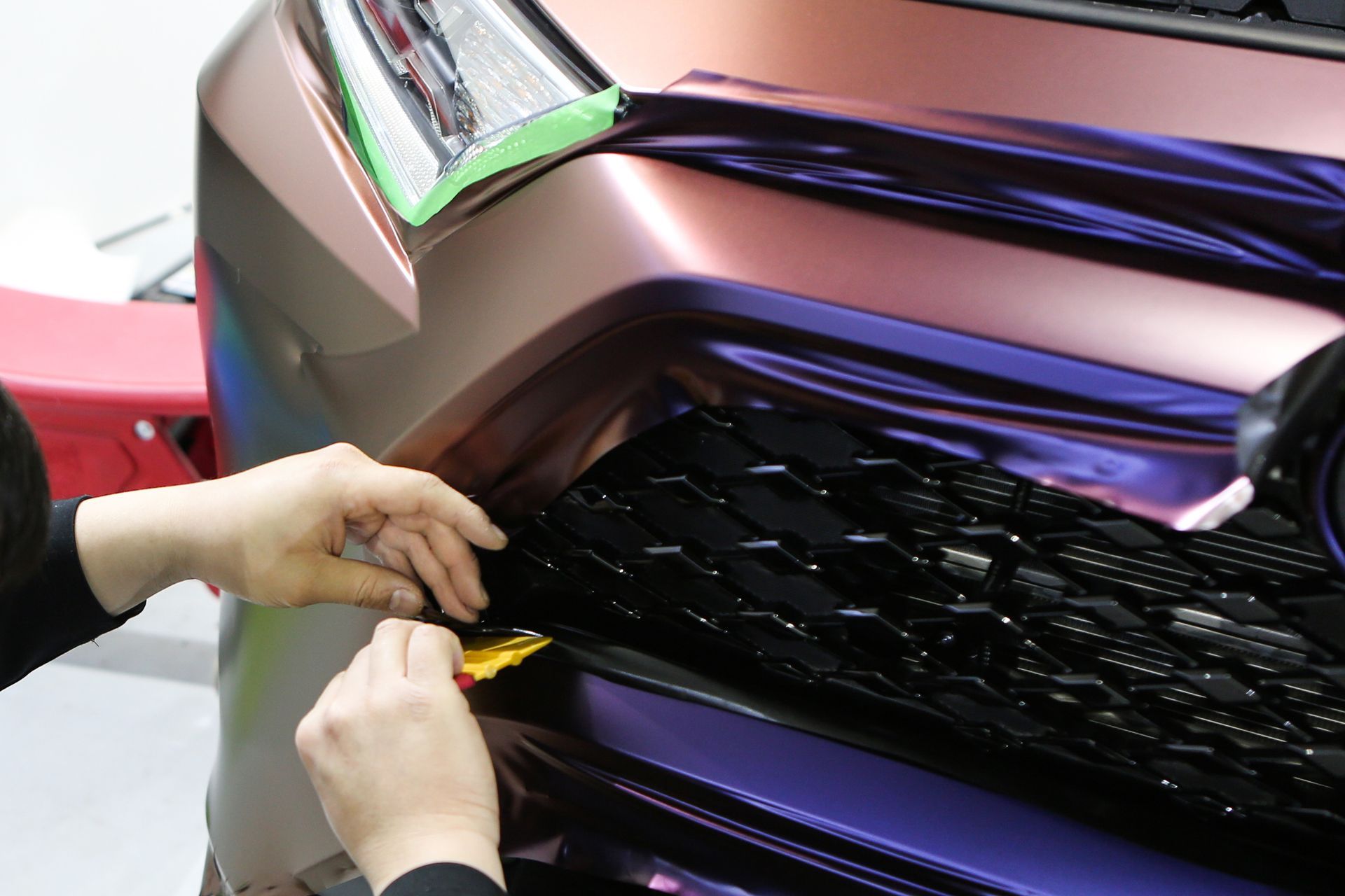 Un car detailer qui réalise les finitions de la pose d'un covering sur une voiture.