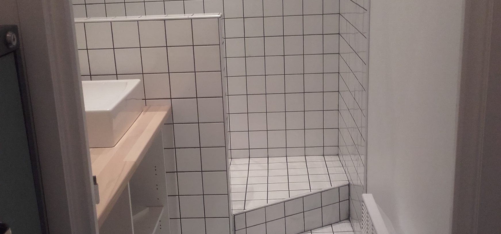 Un seau de ciment, une truelle et une éponge sont posés sur un sol carrelé.