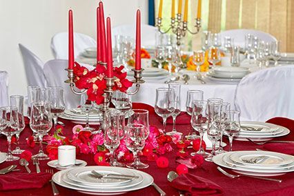 Élégante table dressée pour un événement formel, avec nappe rouge, bougies et verrerie.