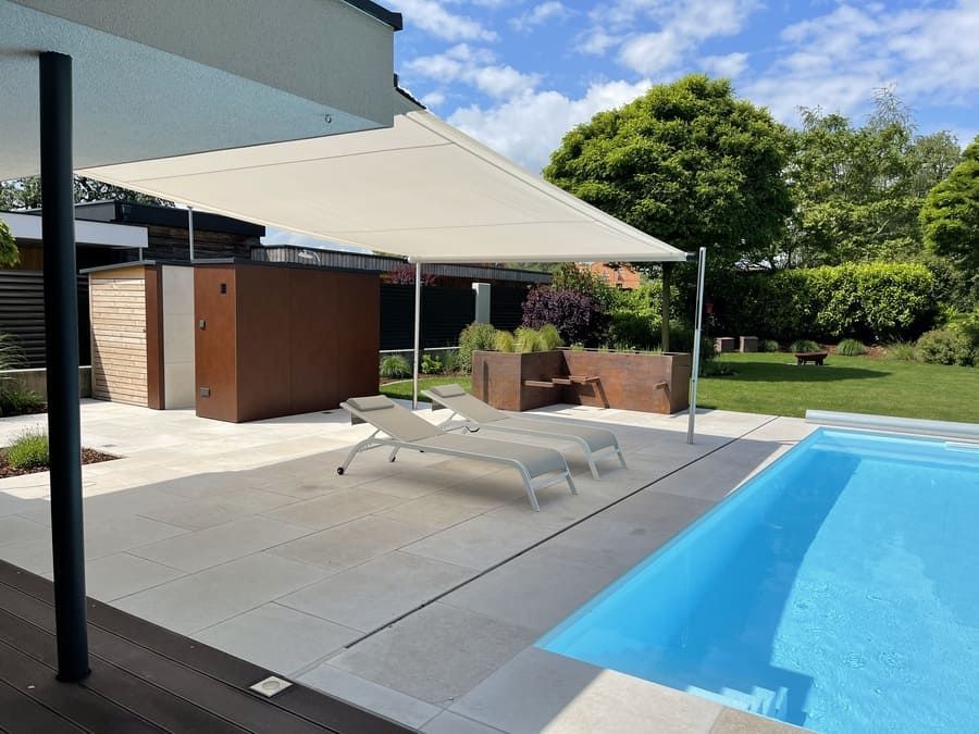 Terrasse au bord de la piscine avec parasol ; chaises longues, piscine et rangement en métal marron.