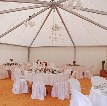 Réception de mariage sous une tente blanche, tables rondes avec centres de table floraux, chaises blanches et un lustre.