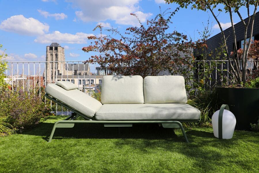 Chaise longue verte d'extérieur sur un toit-terrasse avec ciel bleu et paysage urbain en arrière-plan.